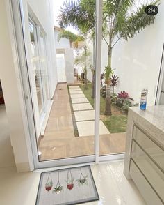 an open door leading to a patio with potted plants on the floor and trees in the background