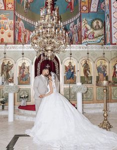 a bride and groom standing in front of a chandelier with paintings on the walls