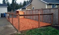 a wooden fence is in front of a house with red mulch on the ground