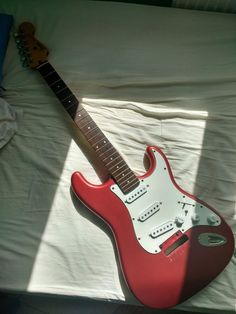 a red electric guitar sitting on top of a bed