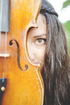 a woman with long hair is looking at the camera while holding a violin in front of her face