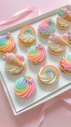 cupcakes decorated with rainbow icing and sprinkles on a white tray