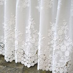 white lace curtains are lined up against a stone wall