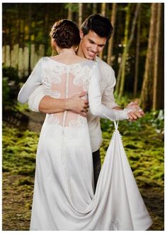 a man and woman dressed in wedding clothes hugging each other while standing in the woods