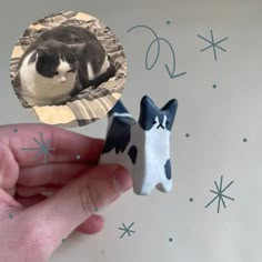 a hand is holding two small cats made out of clay and paper with snowflakes in the background