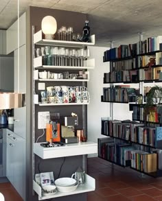 a room filled with lots of books next to a white counter topped with bowls and cups