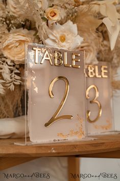 the table numbers are gold and white with flowers in the vases behind them on display