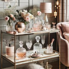 a table topped with lots of bottles and glasses next to a pink chair in front of a window