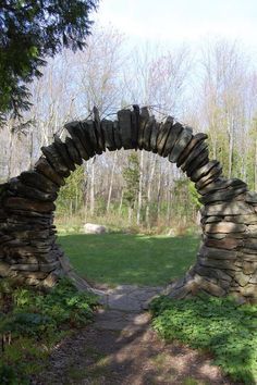 a stone arch in the middle of a grassy area