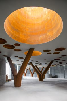 an empty room with round lights on the ceiling and trees in the center, surrounded by concrete pillars