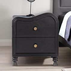 a black night stand with two drawers and a clock on the top, next to a bed