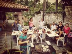 a group of people sitting around a table with food on it and one man standing in front of them