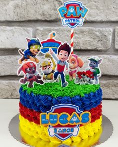 a birthday cake decorated with cartoon characters and the name paw patrol on top is sitting in front of a brick wall