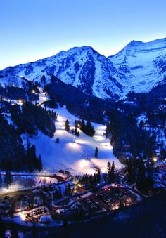 a ski resort at night with snow covered mountains in the background and lights lit up