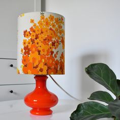 an orange lamp is sitting on a table next to a potted plant