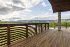 a wooden deck with stone pillars and railings on the side of a house overlooking mountains