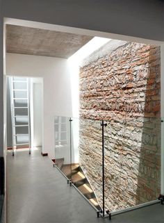 a stone wall in the middle of a room with glass railings and stairs leading up to it