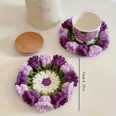 two crocheted coasters sitting on top of a table next to a cup