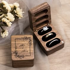 two wooden boxes with wedding rings in them on a table next to some white flowers