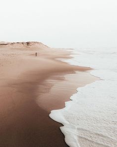 a person walking along the beach in front of an ocean shore line with sand and water