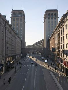 an empty city street with tall buildings and people walking on the sidewalk in front of it