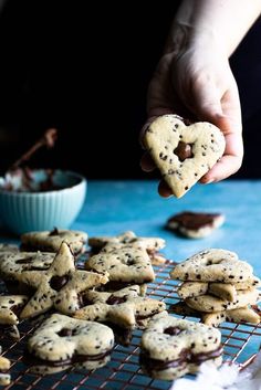 a person holding a heart shaped chocolate chip cookie over a cooling rack full of cookies