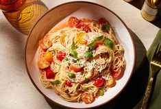 a plate of pasta with tomatoes and parmesan cheese on it next to a glass of wine