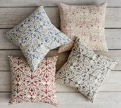 four decorative pillows sitting on top of a wooden floor next to each other and one pillow has an intricate design