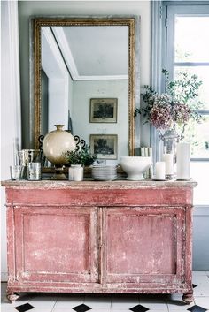 a pink dresser with vases and candles on it in front of a large mirror