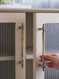 a person is opening the door to their kitchen cabinet with brass handles and knobs