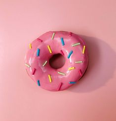 a pink donut with sprinkles on it sitting on a pink surface