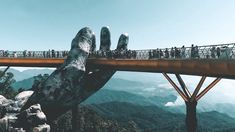 people are standing on a bridge that is high above the water and mountains in the background