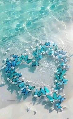 a heart made out of blue butterflies floating in the water on top of a sandy beach