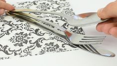 a person holding a fork and knife on top of a white napkin with black damask