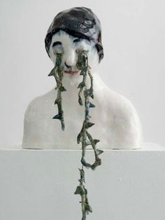 a white sculpture with black hair and spikes attached to it's face, against a white wall