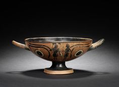 an old bowl with two handles and designs on the side, sitting on a black surface