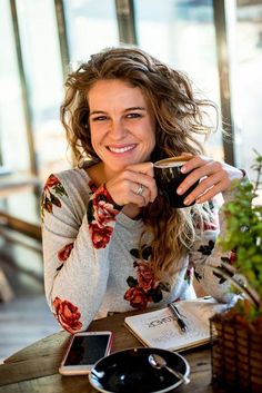 a woman sitting at a table drinking from a cup