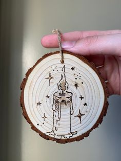 a hand holding a wooden ornament with a drawing on it