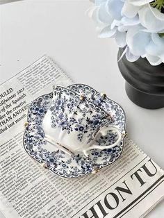 a tea cup and saucer sitting on top of a newspaper next to a vase with flowers