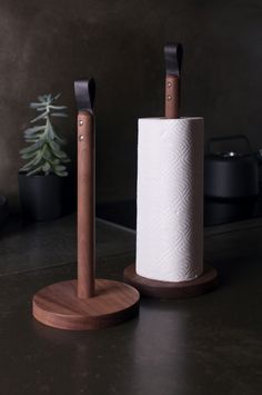 two wooden toilet paper holders on top of a black counter next to a potted plant