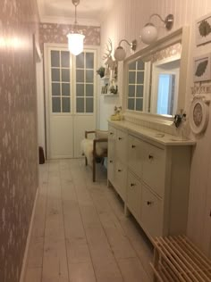 a white bathroom with wooden flooring and wallpaper on the walls, along with a large mirror