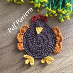 a crocheted turkey sitting on top of a wooden floor next to yellow flowers