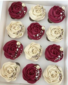 twelve cupcakes in a white box decorated with red and cream frosting roses