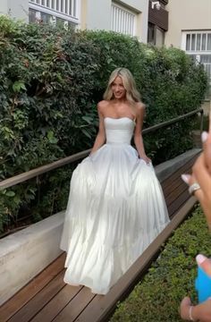 a woman in a white wedding dress taking a selfie with her cell phone while sitting on a bench