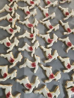 many decorated cookies are on a baking sheet with red sprinkles and white frosting