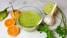 a glass filled with green liquid next to sliced oranges and cilantro