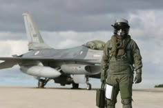 a fighter jet sitting on top of an airport tarmac next to a man in uniform