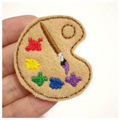 a hand holding a small embroidered patch with an image of a fishing hook