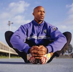 a man sitting on the ground with his hands in his pockets and wearing a blue jacket