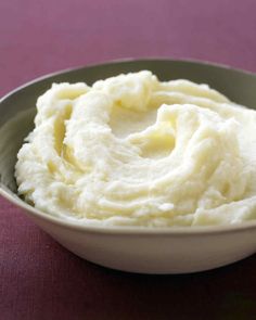 a bowl filled with mashed potatoes sitting on top of a purple tablecloth covered table